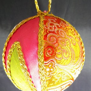 Puede incluir: Un adorno navide&ntilde;o hecho a mano en forma de esfera, hecho de tela rosa, verde y dorada con un ribete de trenza dorada. El adorno tiene un dise&ntilde;o tradicional y es perfecto para agregar un toque de elegancia a tu decoraci&oacute;n navide&ntilde;a.