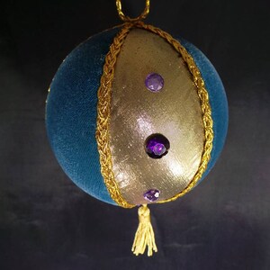 Puede incluir: Un adorno navide&ntilde;o de terciopelo azul y dorado con un borla dorada y diamantes de imitaci&oacute;n morados.