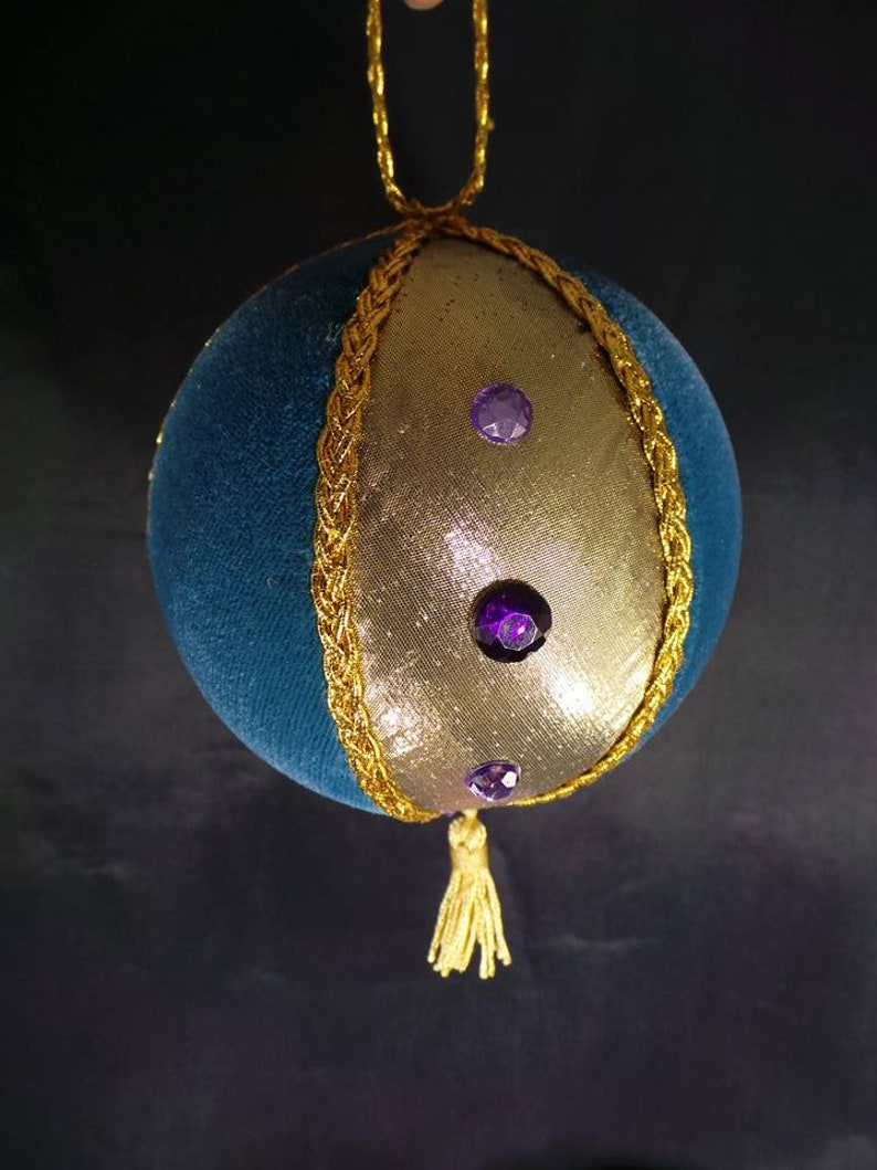 Puede incluir: Un adorno navide&ntilde;o de terciopelo azul y dorado con un borla dorada y diamantes de imitaci&oacute;n morados.