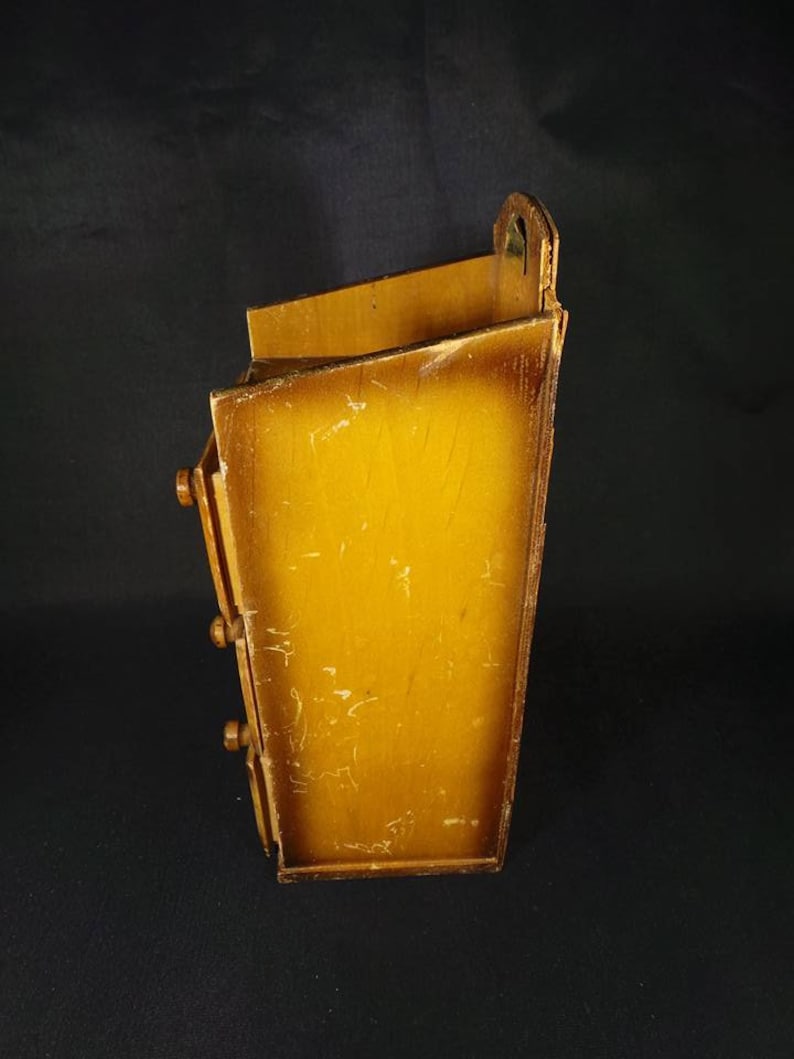 May include: A wooden wall mounted organizer with three drawers. The organizer is stained a light brown color and has a brass handle on the top.