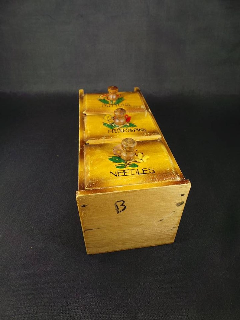 May include: Wooden box with three drawers for storing sewing supplies. The drawers are labeled "Buttons", "Needles & Pins", and "Needles".