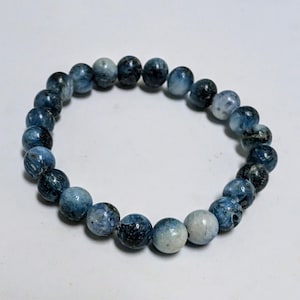 May include: A blue gemstone bracelet with round beads. The beads have a mottled blue and white pattern.
