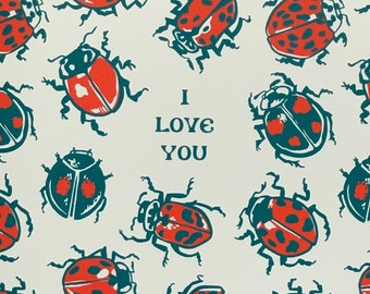 May include: Greeting card with a cream background and a pattern of red and teal ladybugs. The words "I Love You" are printed in black. The card is in a brown envelope, set against a red background.