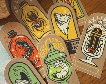 May include: Set of seven "Ex Libris" bookplates with illustrations of insects and creatures in jars. The bookplates are printed on brown cardstock with a variety of colors, including yellow, orange, and green. The text "Ex Libris" is printed on each bookplate.