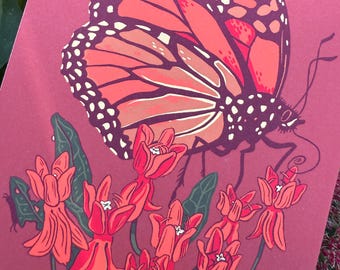 May include: A print featuring a monarch butterfly with orange and black wings, perched above red flowers with green leaves. The background is a deep red color, with a hint of green foliage.
