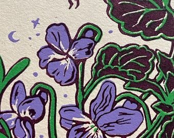 May include: A detailed illustration of violets and foliage in shades of purple, green, and burgundy. A green insect hovers above the flowers, with a crescent moon and stars in the background. The artwork has a vintage, botanical feel.