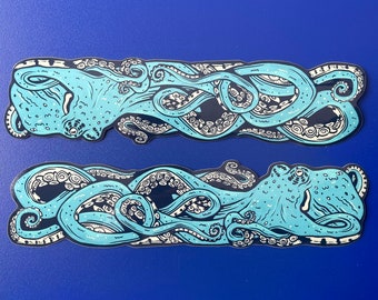 May include: Two rectangular stickers featuring a teal octopus design with dark blue and white accents. The octopus has detailed tentacles and is set against a dark blue background. The stickers are on a blue surface.