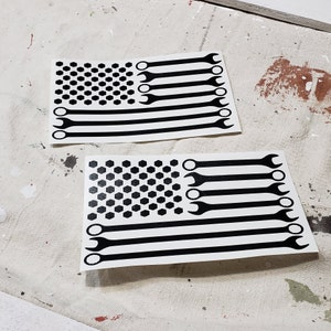 May include: Two black and white vinyl decals of the American flag with wrench designs. The wrench designs are in place of the red stripes on the flag.