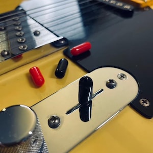 Op de afbeelding: Close-up van een gele elektrische gitaar met zwarte en rode knoppen, een zwarte schakelaar en een chromen bedieningspaneel.