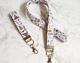May include: Two white fabric lanyards with a Harry Potter theme. The lanyards feature a white background with illustrations of glasses, wands, letters, and a hat. The lanyards have silver key rings attached.