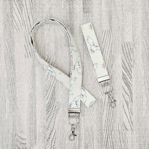 May include: A light green lanyard and wrist strap with a repeating pattern of white owls carrying mail. Both accessories have silver-coloured metal hardware, including a lobster clasp and a key ring.