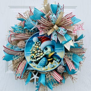 May include: A festive Christmas wreath featuring a central circular image of a cartoon turtle wearing a Santa hat and a seashell Christmas tree. The wreath is adorned with turquoise, red, and gold ribbons, starfish, and decorative balls. The text "Merry & Bright" is visible.
