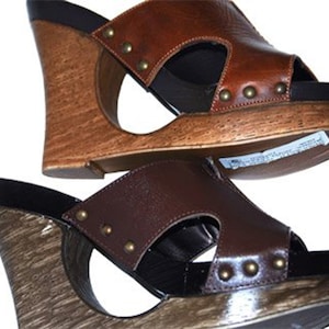 May include: Two pairs of brown leather wedge sandals with a cutout design and studded accents. The sandals have a wooden wedge heel.