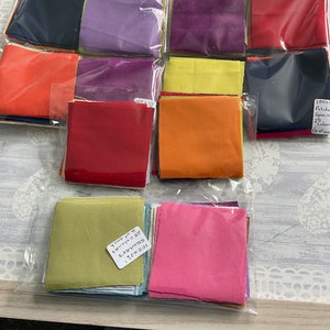 May include: A collection of 100x100 inch fabric squares in various colours, including red, orange, yellow, green, blue, purple, and pink. The squares are packaged in clear plastic bags and labelled "100x100 Squares 25 Colours 1 inch each".