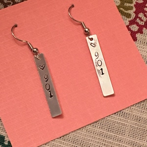 May include: A pair of silver earrings with a rectangular charm that says "901" with a heart symbol above the number.