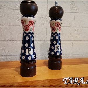 Peut inclure: Une paire de moulins à sel et à poivre en céramique. Les moulins ont une base et un dessus en bois foncé avec un motif floral blanc et bleu. La lettre "P" est sur un moulin et "S" sur l'autre.