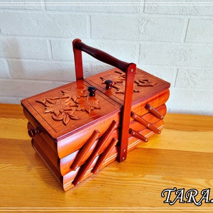 May include: A wooden sewing box with a hinged lid and a carved floral design. The box has a handle and is made of multiple layers of wood.
