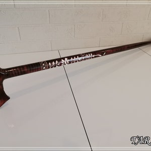 May include: A brown wooden walking stick with a white floral design and a black rubber tip. The stick has a T-shaped handle.