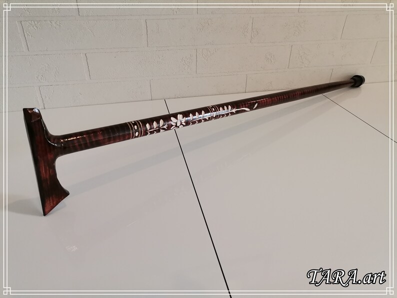 May include: A brown wooden walking stick with a white floral design and a black rubber tip. The stick has a T-shaped handle.