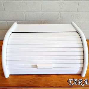 Puede incluir: Caja de pan de madera blanca con tapa enrollable. La tapa tiene una pequeña manija.