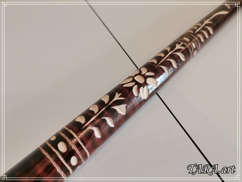 May include: A wooden walking stick with intricate white floral carvings. The stick is dark brown with a glossy finish. The carvings are detailed and delicate, creating a beautiful pattern.