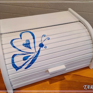 May include: White wooden bread bin with a blue butterfly design. The butterfly has a heart shape in the centre of its wings.