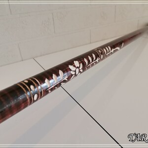 May include: A wooden walking stick with a dark brown stain and white floral carvings. The stick has a black rubber tip.