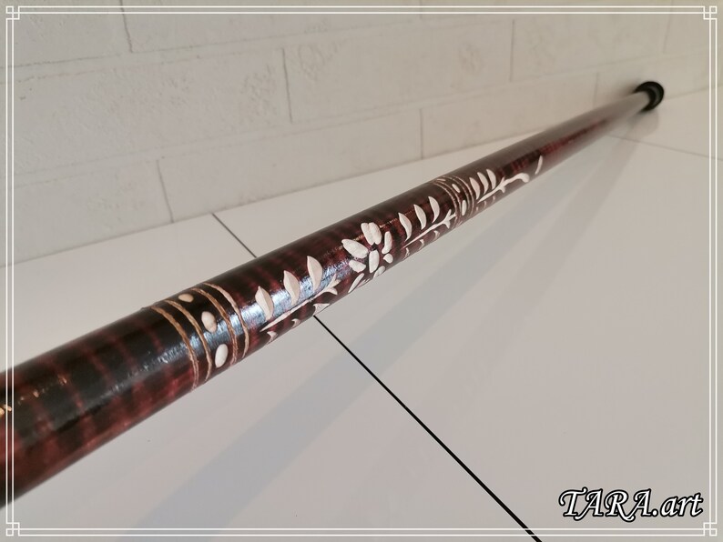 May include: A wooden walking stick with a dark brown stain and white floral carvings. The stick has a black rubber tip.