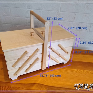 May include: A wooden sewing box with a hinged lid and a handle. The box has four compartments and is 15.75 inches wide, 7.87 inches deep, and 13 inches tall. The box is made of light wood and has a natural finish.