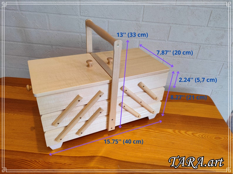 May include: A wooden sewing box with a hinged lid and a handle. The box has four compartments and is 15.75 inches wide, 7.87 inches deep, and 13 inches tall. The box is made of light wood and has a natural finish.