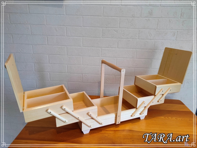 May include: A wooden sewing box with four compartments and a handle. The box is open and the compartments are visible. The box is made of light wood and has a natural finish.