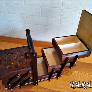 May include: A wooden sewing box with three drawers and a carved floral design on the top. The box has a handle and is open to reveal the empty drawers.
