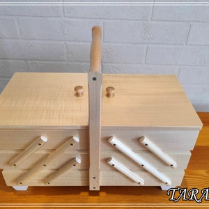 May include: A wooden sewing box with a hinged lid and a handle. The box has multiple compartments and is decorated with white wooden dowels.
