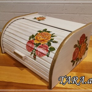 Puede incluir: Caja de pan de madera blanca con tapa enrollable. La caja está decorada con rosas amarillas y rosas pintadas. El texto "TARA.art" es visible en la esquina inferior derecha de la caja.