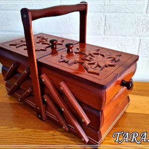 May include: A wooden sewing box with a hinged lid and a carved sunflower design. The box has a handle and is made of dark wood.