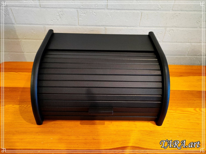 May include: A black wooden bread box with a roll-top lid. The lid has a series of horizontal slats that slide up and down.