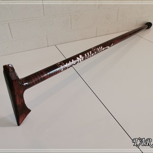 May include: A wooden walking stick with a carved floral design and a dark brown stain. The stick has a T-shaped handle.