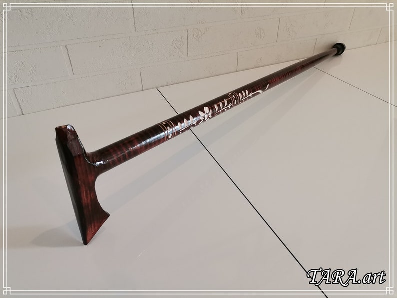 May include: A wooden walking stick with a carved floral design and a dark brown stain. The stick has a T-shaped handle.