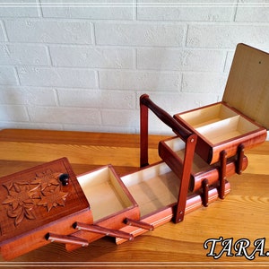 May include: A wooden sewing box with three drawers and a hinged lid. The top drawer features a carved floral design. The box is open and the drawers are pulled out.