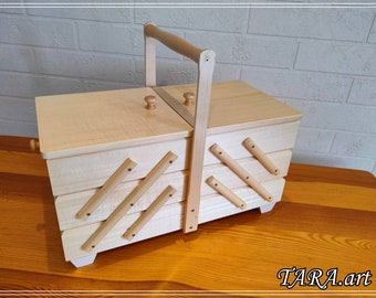 May include: A wooden sewing box with a hinged lid and a handle. The box has four compartments and is decorated with wooden slats.