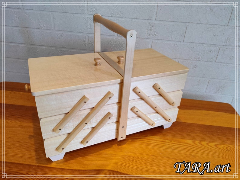 May include: A wooden sewing box with a hinged lid and a handle. The box has four compartments and is decorated with wooden slats.