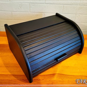 May include: Black wooden bread box with a roll-top lid. The lid has a slatted design and a small handle.
