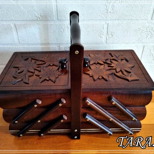 May include: A wooden sewing box with a carved floral design and a handle. The box has three compartments and is made of dark wood.
