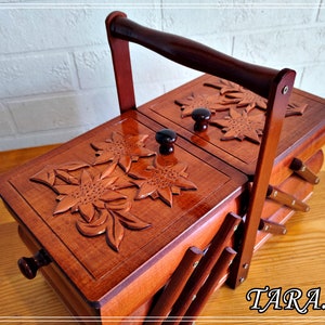 May include: A wooden sewing box with a hinged lid and a carved floral design. The box has a handle and is made of light brown wood.