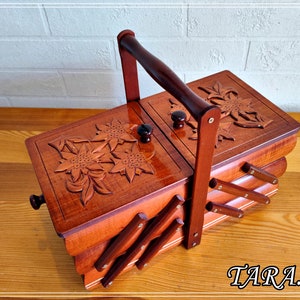 May include: A wooden sewing box with a hinged lid and a carved floral design. The box has a handle and is made of multiple layers of wood.
