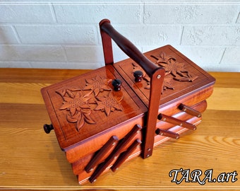 May include: A wooden sewing box with a hinged lid and a carved floral design. The box has a handle and is made of multiple layers of wood.