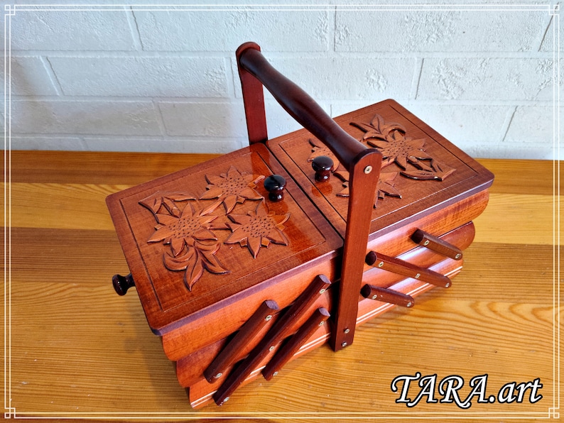 May include: A wooden sewing box with a hinged lid and a carved floral design. The box has a handle and is made of multiple layers of wood.