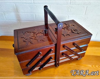 May include: A wooden sewing box with a hinged lid and a carrying handle. The box has three compartments and is decorated with carved floral designs.