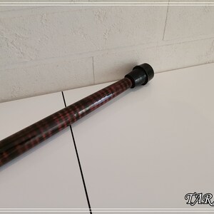 May include: A wooden walking stick with a black rubber tip. The stick has a dark brown stain with a red and black pattern.