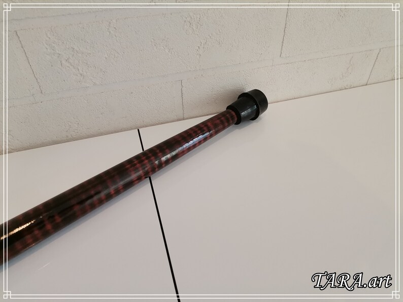 May include: A wooden walking stick with a black rubber tip. The stick has a dark brown stain with a red and black pattern.